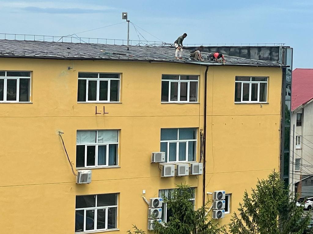 Echipă montaj acoperiș pe bloc cu fațadă galbenă